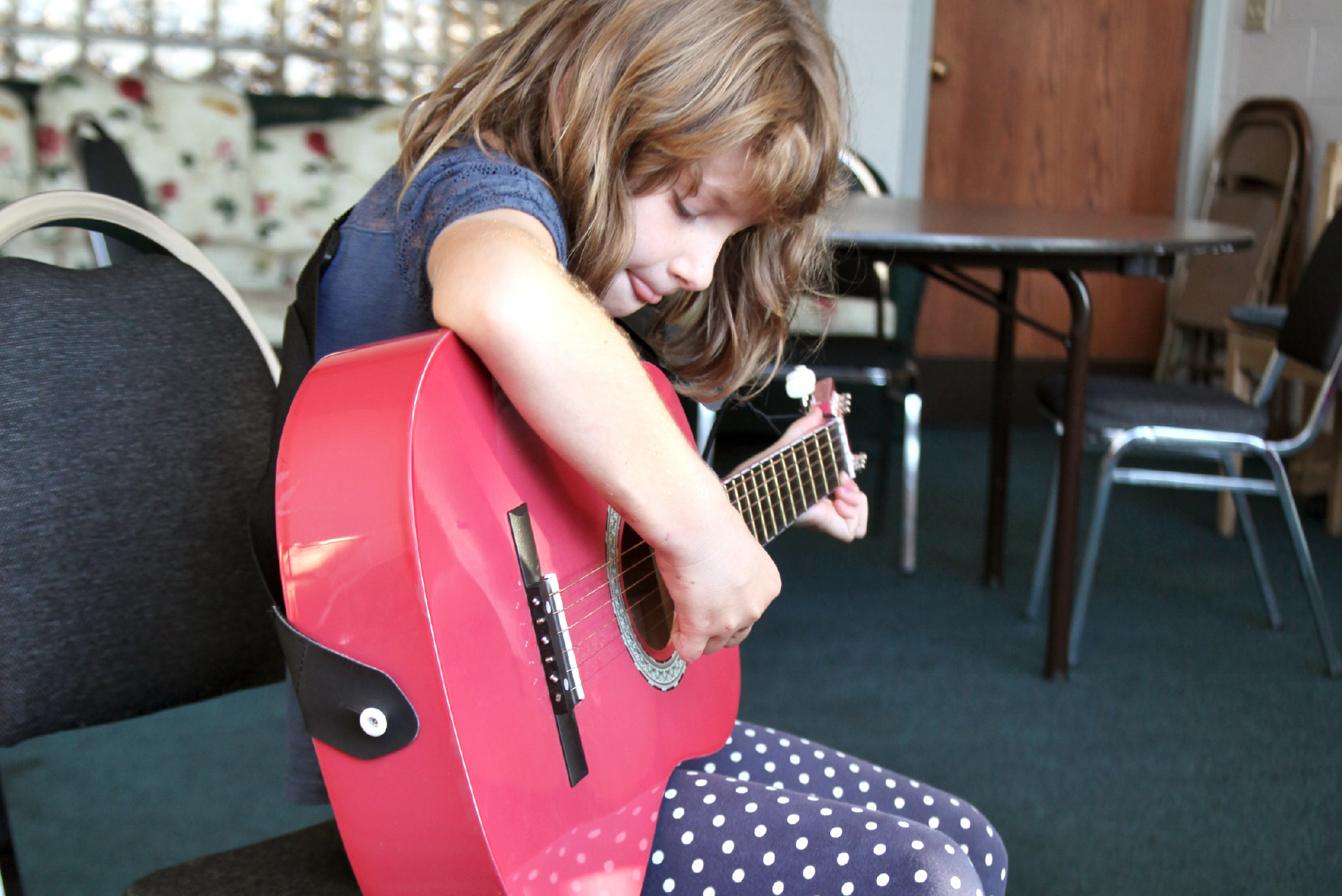 A young girl plays a pink guitar.