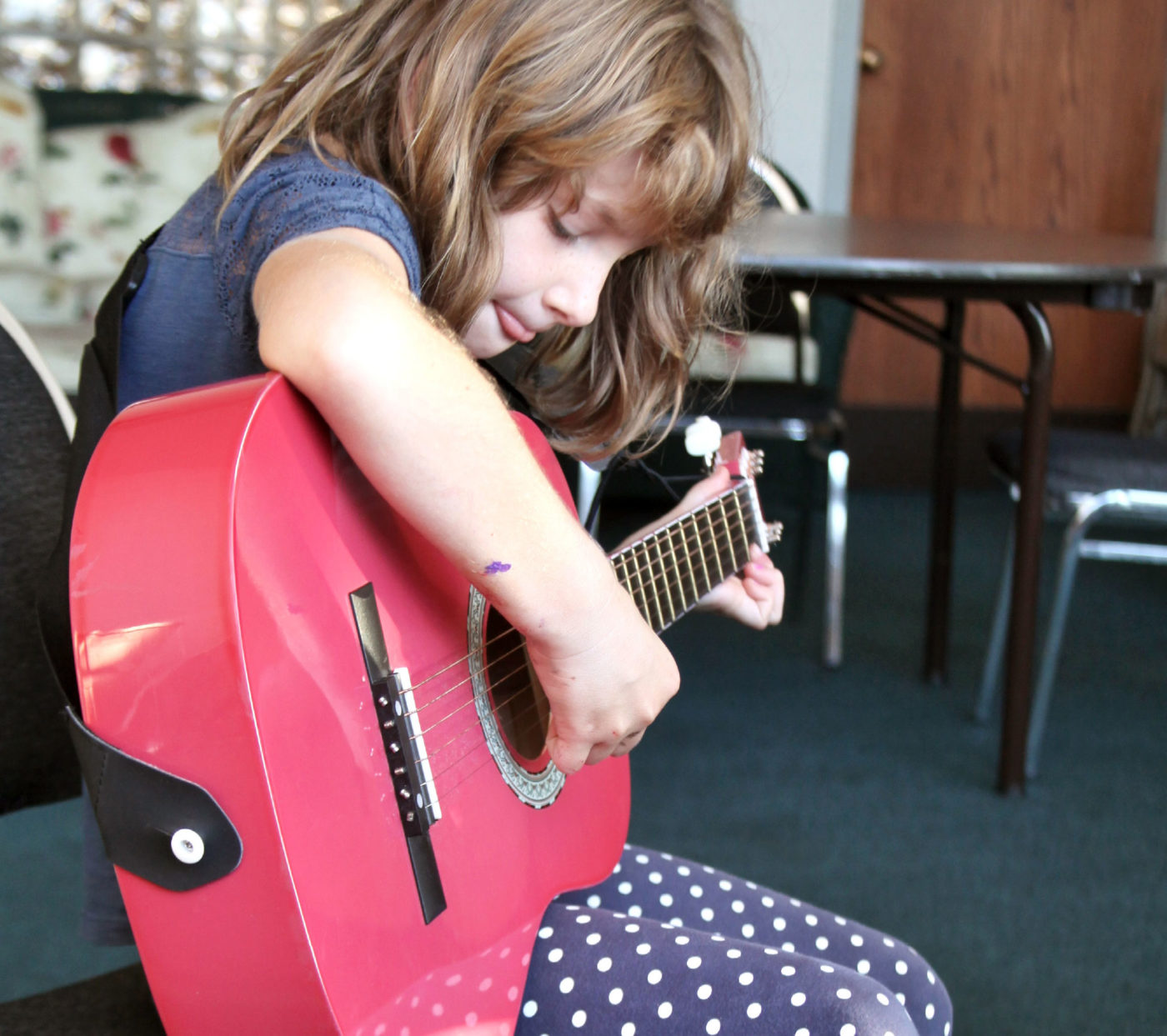 A young girl plays a pink guitar.