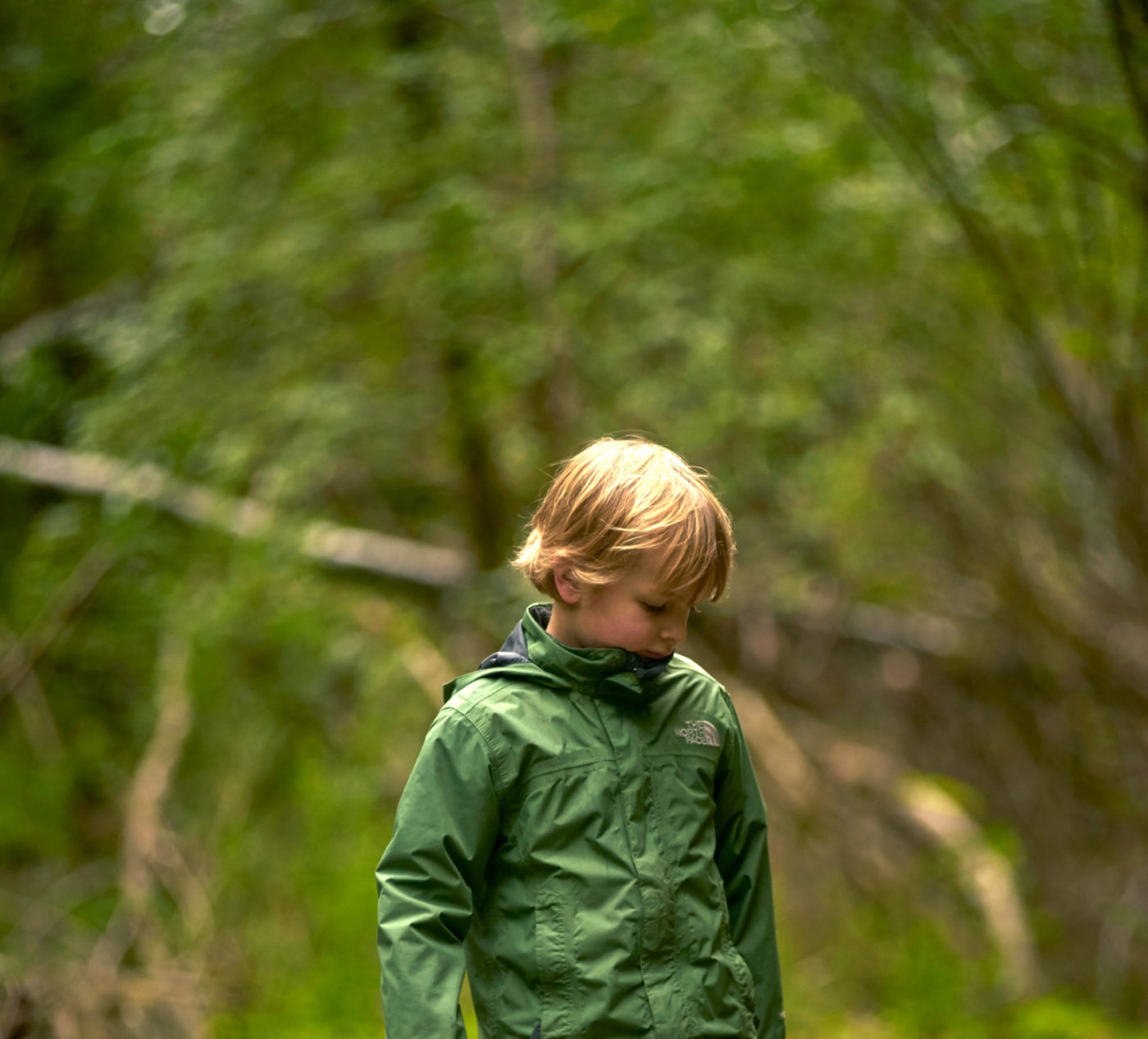 A young boy with blond hair dressed in a green jacket walks down a trail at the quarry.