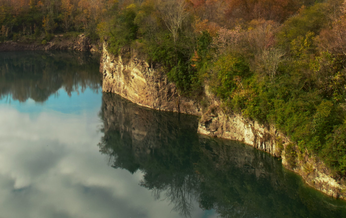 A view overlooking sheer face of the quarry and the lake below, which reflects the sky.