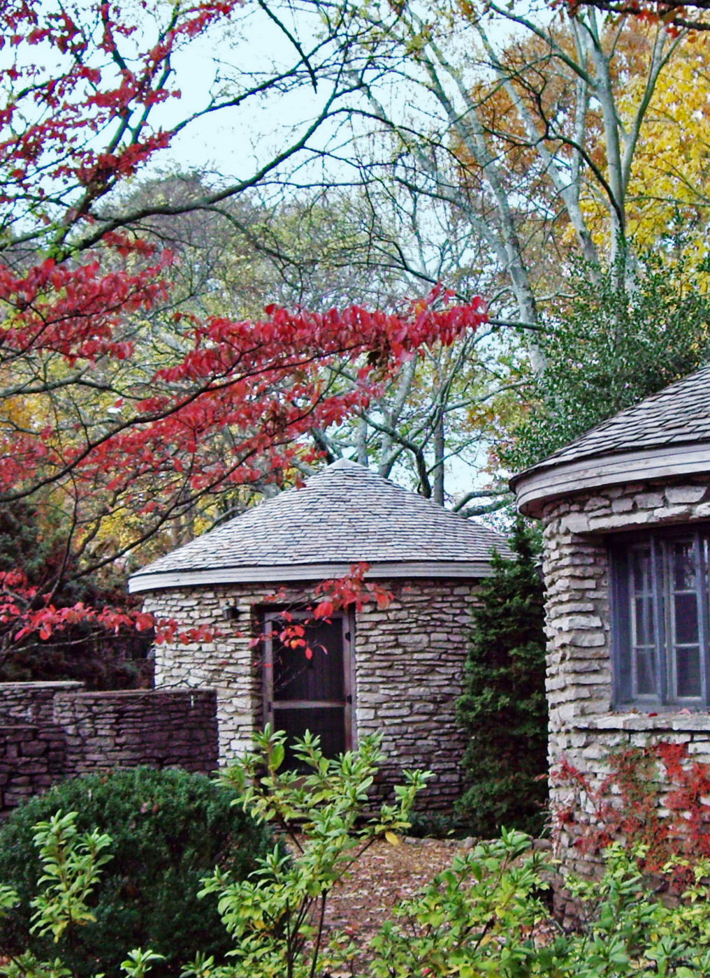 A photo shows the stone buildings at the arboretum surrounded by trees and bushes.
