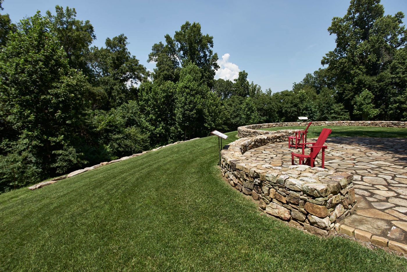 Red chairs on a stone embankment overlook a grassy sloping hill.