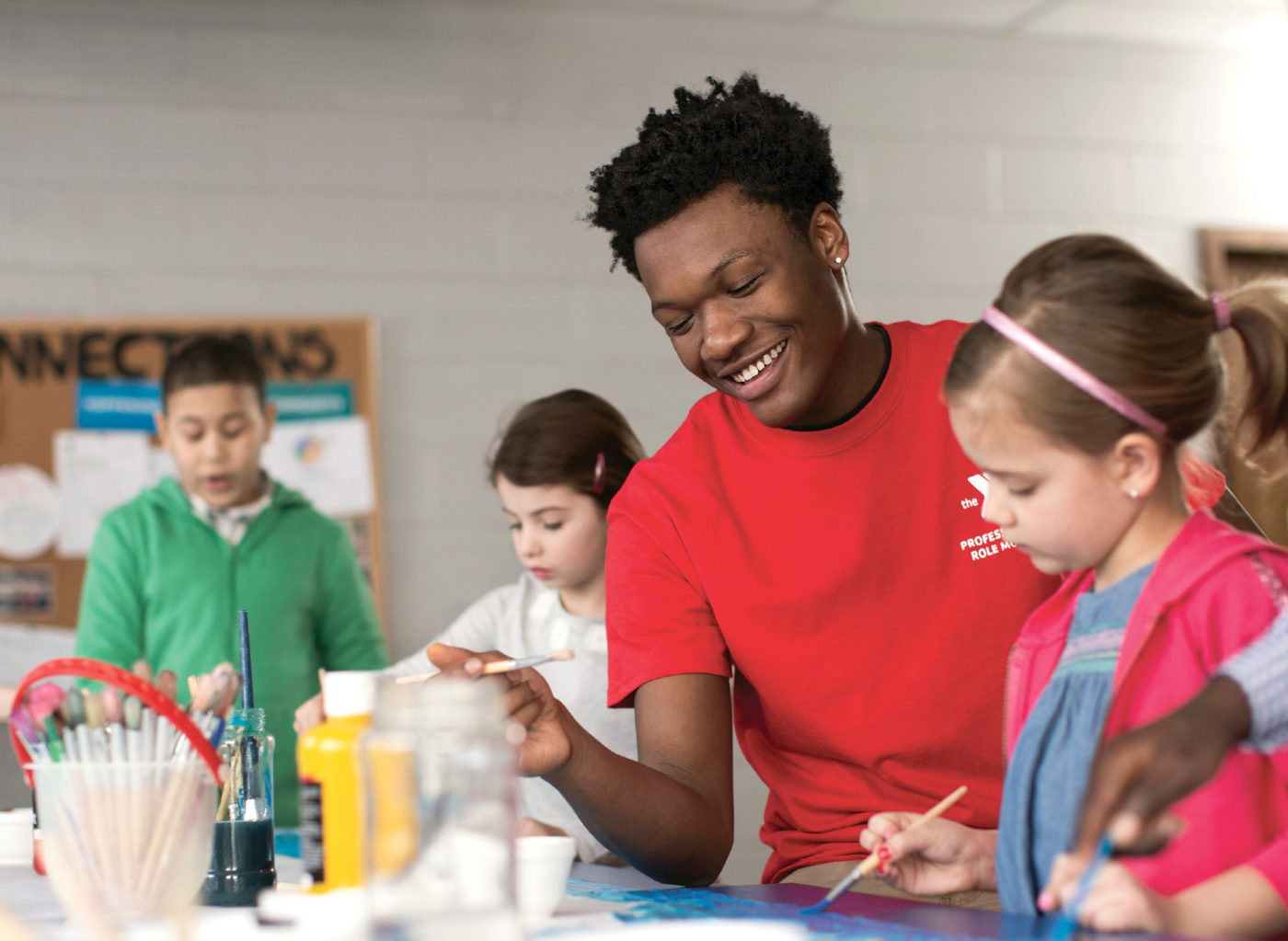 An instructor demonstrates an art project to young children inside a classroom.