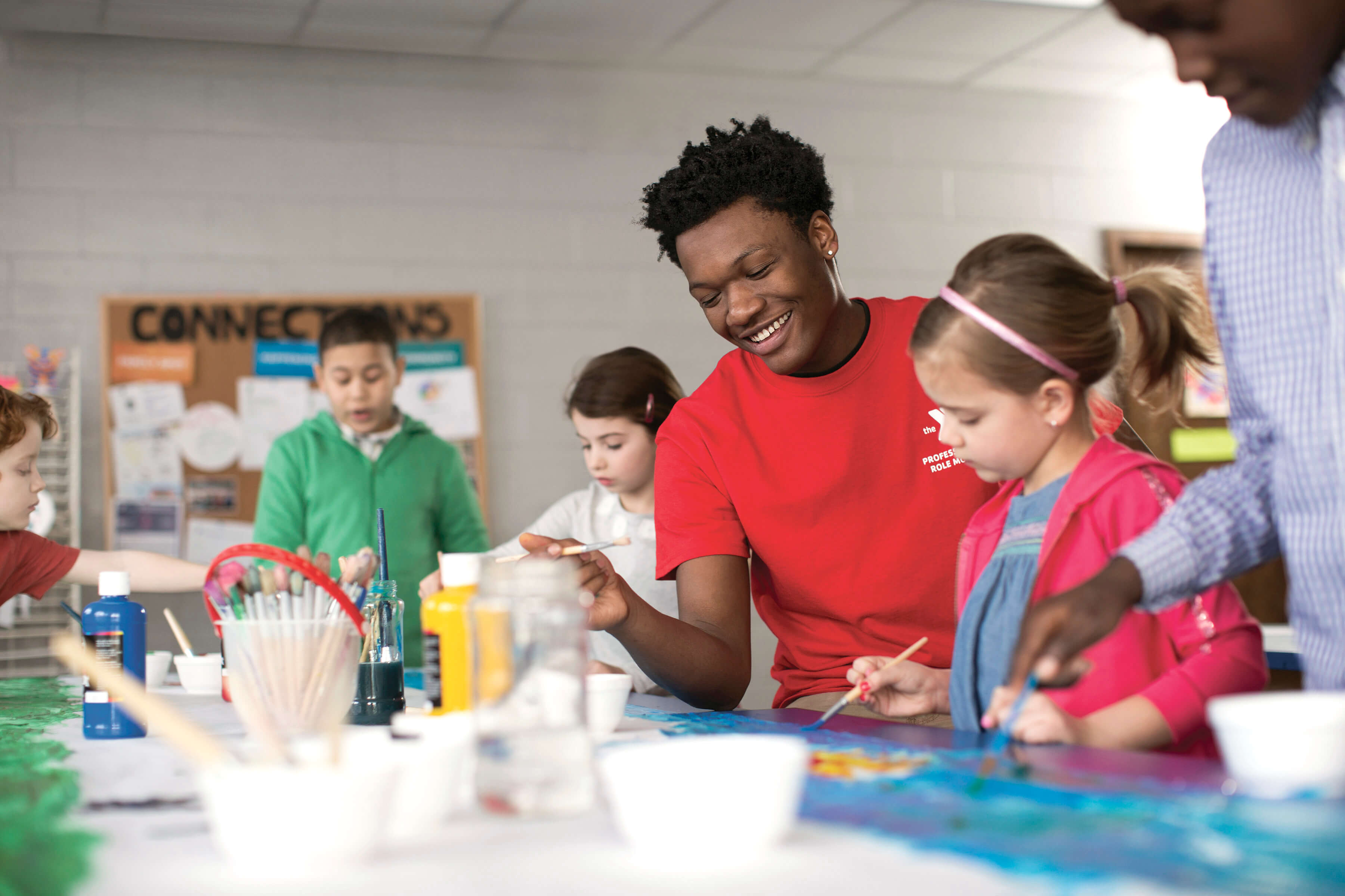 An instructor demonstrates an art project to young children inside a classroom.