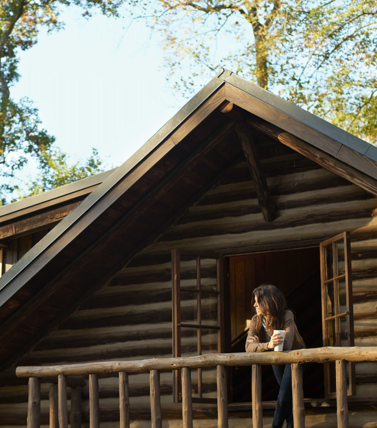 An artist leans on the rustic railing of a cabin balcony.