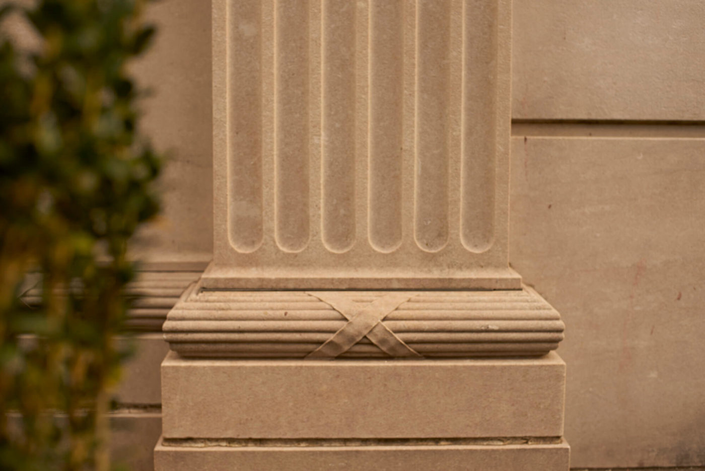 A photo of the base of an engaged fluted column, carved in marble, on the exterior of the building.