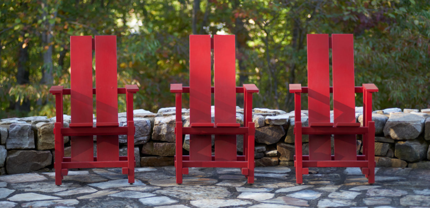 A photo of three red-painted Adirondack chairs at High Ground Park.