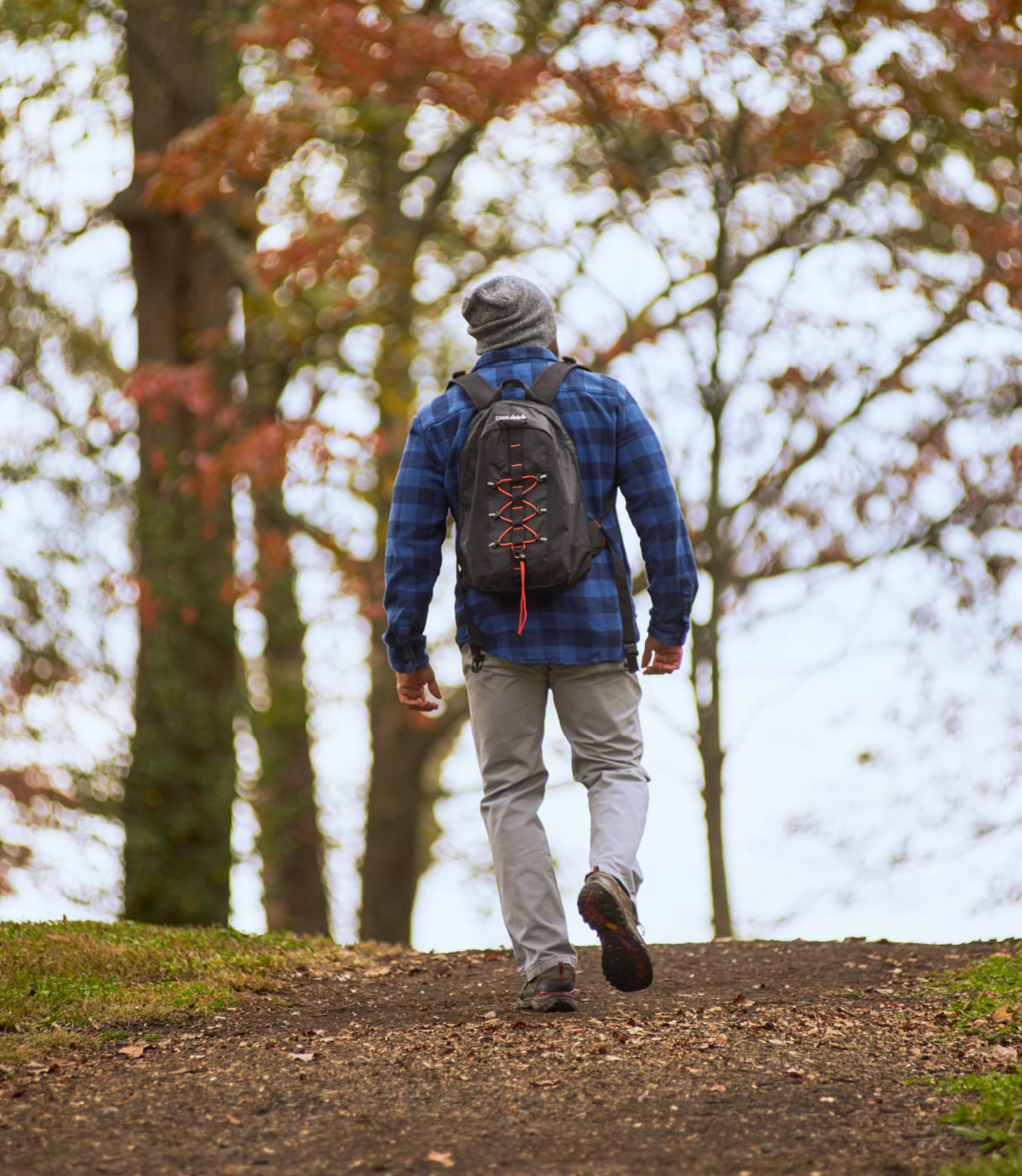 A man wearing a blue plaid shirt and a backpack walks down a trail at Fort Dickerson.