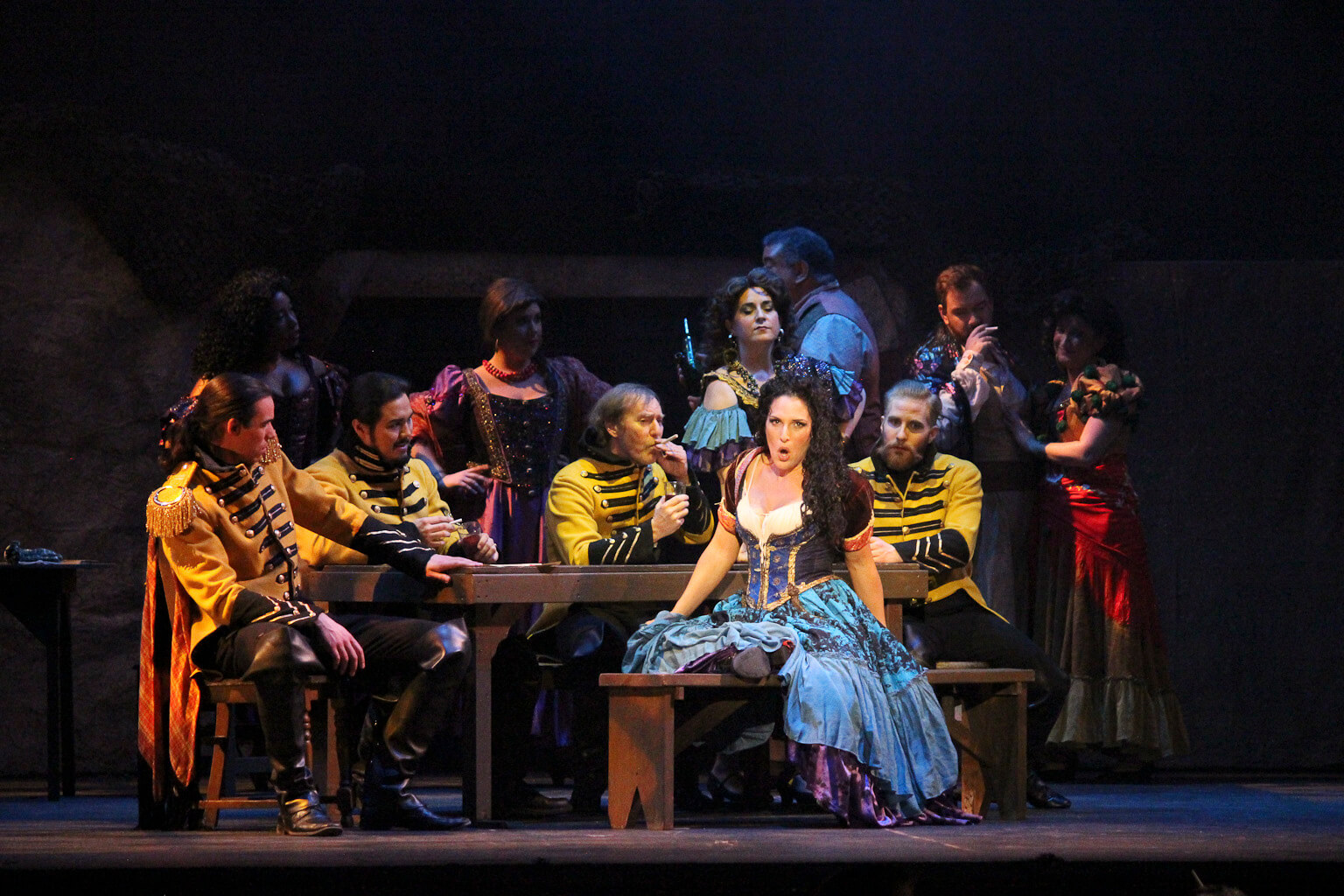 A soprano and cast members in 19th-century costume perform an opera onstage.