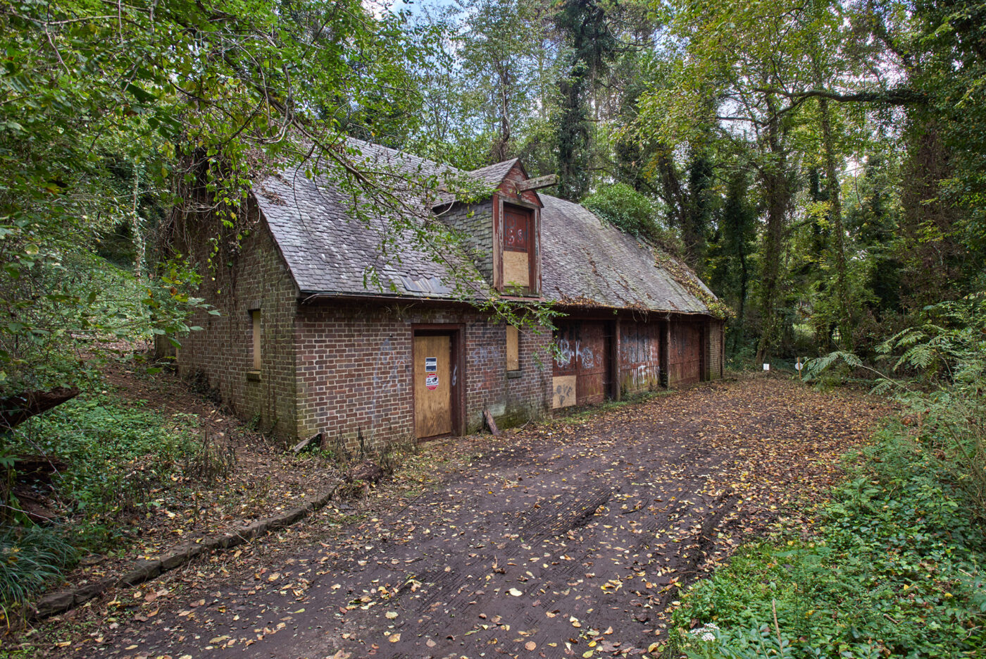 A carriage house building in pre-restoration condition sits at the end of a path in the woods.