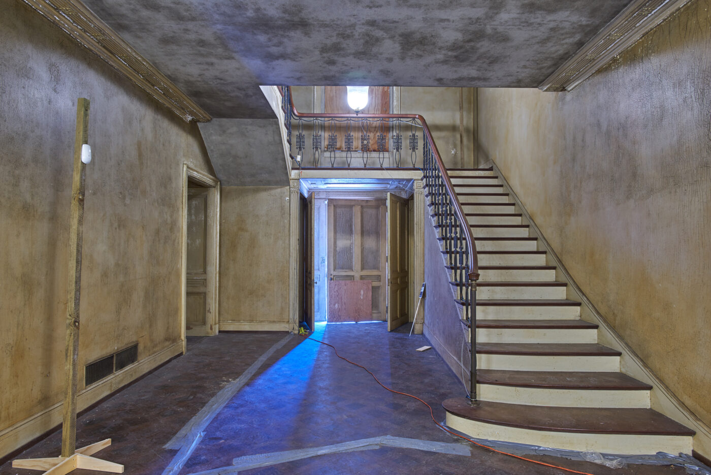 A view of the grand foyer, looking up the central staircase and the front door. The room is in pre-restoration condition.