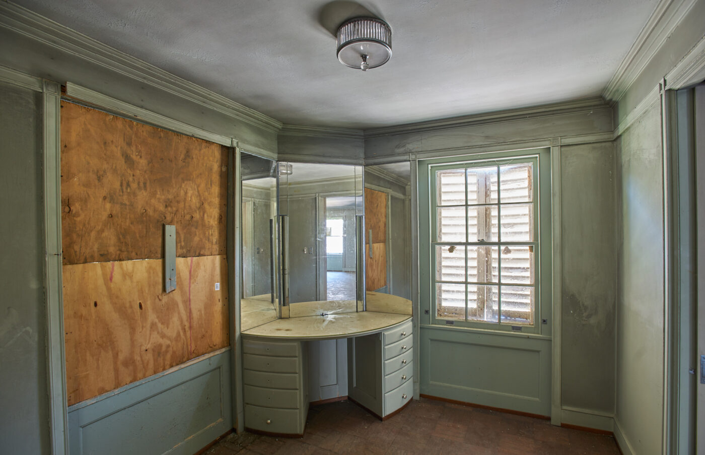 A photo of the dressing room in pre-restoration condition, which has boarded up windows and pale green walls.